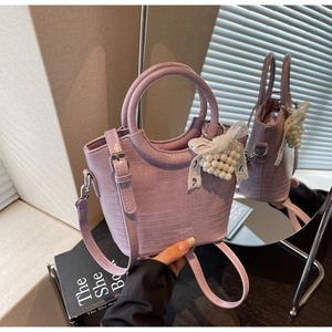 Detail of purple crocodile texture bucket bag with pearl and lace bow charm on mirror
