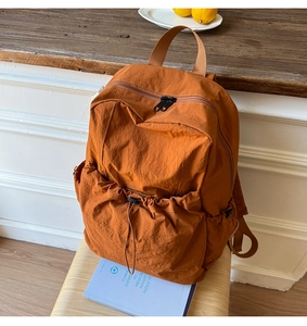 Detail of orange-brown nylon backpack featuring a drawstring front pocket on a wooden chair