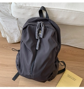Detail of dark grey backpack with vertical zipper and textured woven cord pullers