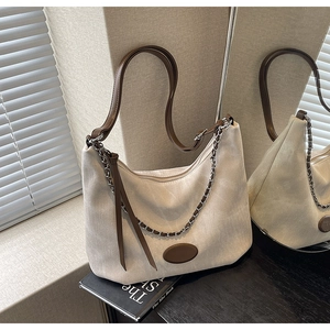 Detailansicht der beigen Canvas-Schultertasche mit braunem Lederbesatz und Kette