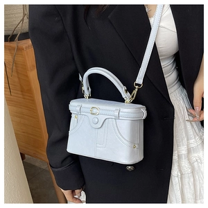 Detail showing a light blue box crossbody bag with button decor worn with a black blazer