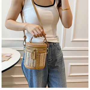Detail of a cylindrical straw crossbody bag with contrast stitching and dual zippers