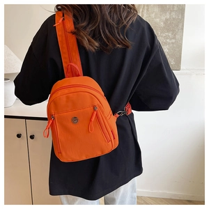 Detail der leuchtend orangefarbenen Nylontasche mit Metalllogo und Reißverschluss