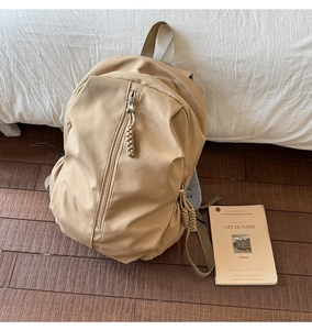 Detail of khaki nylon backpack featuring vertical zipper pocket and woven rope pullers