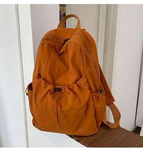 Close-up of rust-red nylon backpack featuring drawstring pocket and matte hardware