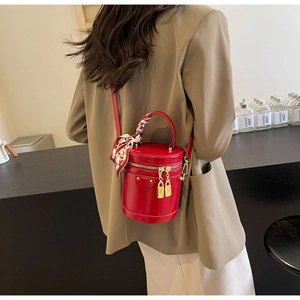Detail view of red cylindrical bucket bag with decorative silk scarf and gold zippers