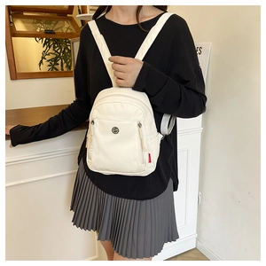 Nahaufnahme eines weißen Nylon-Minirucksacks mit Metalllogo und verstellbaren Schultergurten