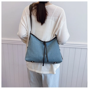 Blue denim tote bag with black leather trim and drawstring detail shown on a model