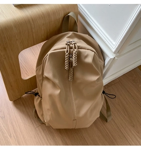 Detail of khaki nylon backpack with vertical zipper and woven rope knot on wooden stool