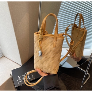 Détail du mini sac seau tressé avec poignées en cuir et breloque haricot argentée sur miroir