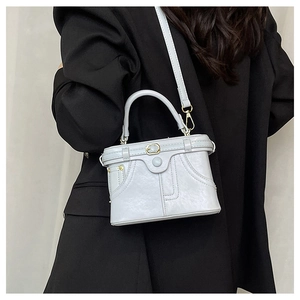 Detail view of light grey matte leather handbag featuring decorative stitching and hardware