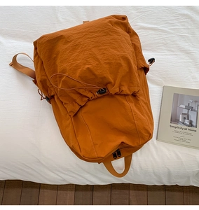 Flat lay of orange nylon backpack with drawstring closure next to a minimalist book
