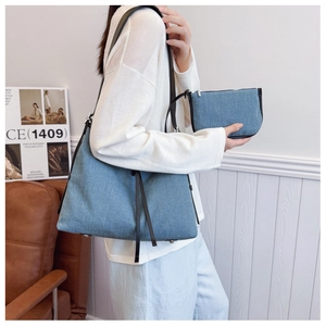 Denim tote bag set with matching zipper pouch and black leather straps shown on a model
