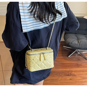 Detail of yellow quilted box bag with rhinestones and chain strap on shoulder
