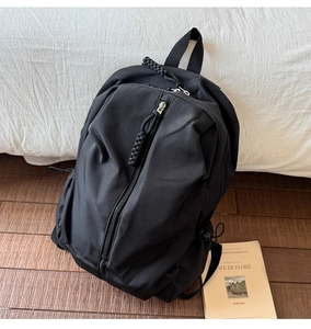 Detail of minimalist black nylon backpack with woven rope zipper pull on white fabric