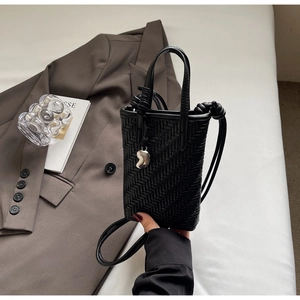 Détail du mini sac seau tressé noir avec breloque cœur argentée et texture cuir