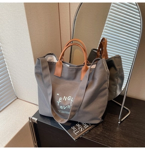Détail du sac fourre-tout en toile grise avec poignées en cuir marron sur bois