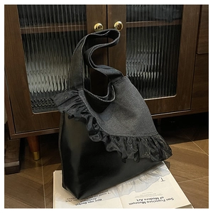 Detail view of denim and leather tote bag featuring elegant black mesh ruffle trim decoration