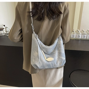 Detail of light blue denim hobo bag with silver chain strap shown on a shoulder