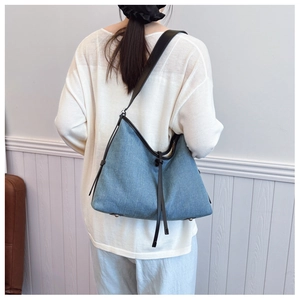 Detail view of a denim tote bag with leather trim and drawstring in a casual styling