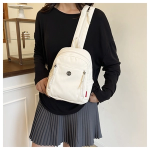Détail d'un mini sac à dos en nylon blanc avec logo smiley en métal et étiquette rouge tissée