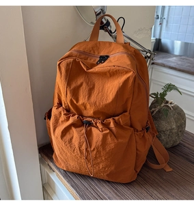 Detail view of orange nylon backpack showing drawstring pocket and dual zipper main compartment