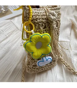 Dettaglio di un ciondolo a fiore giallo con cordoncino a spirale su borsa in paglia