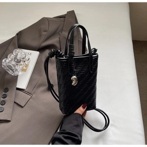 Détail du mini sac seau tressé noir avec un pendentif décoratif en métal argenté
