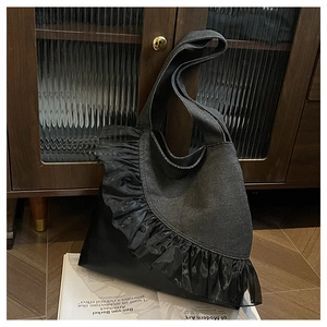 Detail of black denim tote bag featuring translucent organza ruffles and leather base