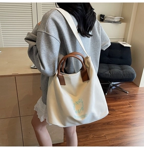Détail du sac cabas en toile blanc cassé avec broderie verte et poignée en cuir marron