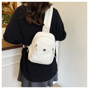 Détail du sac à dos en cuir blanc avec logo métallique rond GM et poche zippée avant