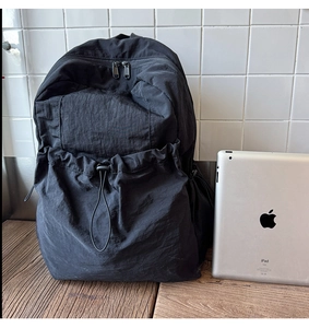Detail of black nylon backpack with drawstring pocket showing size capacity next to iPad