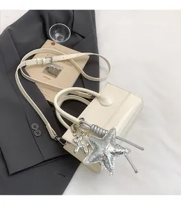 Detail view of cream crossbody bag with silver star and balloon dog charm accessories