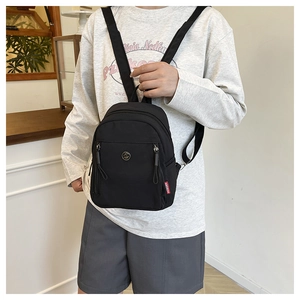 Détail d'un petit sac à dos en nylon noir avec logo GM en métal et étiquette HOBORN rouge