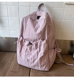 Detail of light purple nylon backpack featuring a drawstring front pocket and textured fabric