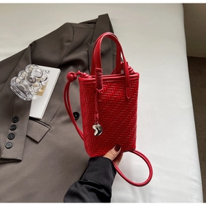 Détail du sac à main tressé rouge avec pendentif cœur et bandoulière réglable