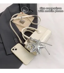 Size comparison of a beige leather crossbody bag with a smartphone and star charm