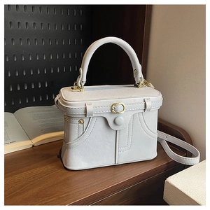 Detail of light gray box bag featuring pocket stitching and elegant metal buckle