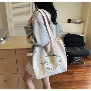 Close-up of a white canvas tote bag featuring green lettering and a drawstring closure