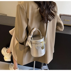 Detail of silver bucket bag with silk scarf handle and adjustable strap on a dark surface