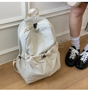 Detailed view of cream nylon backpack with functional drawstring pockets and metal zippers