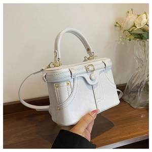 Detail of white box bag featuring denim pocket stitching, metal rivets and gold buckle