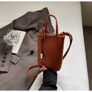 Détail d'un mini sac cabas marron tressé avec pendentif argenté et bandoulière en cuir
