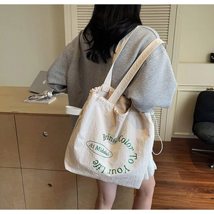 Detail of cream canvas tote bag featuring green circular text and drawstring closure
