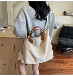 Detailed close-up of ivory canvas tote with brown leather handles and brand embroidery