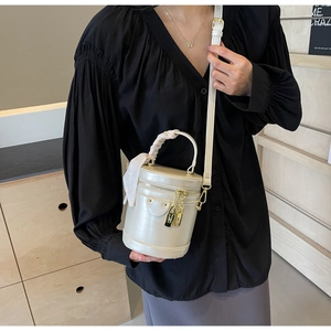 Detail of off-white cylindrical bucket bag with decorative scarf handle and gold lock pendant