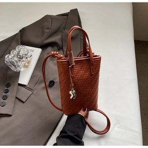 Détail d'un mini sac seau tressé marron avec breloque cœur argentée et texture en cuir