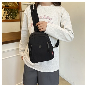 Détail d'un sac bandoulière en nylon noir avec poches zippées et logo métallique rond