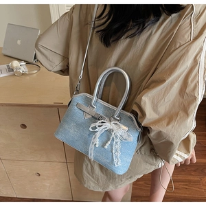Détail d'un sac en denim bleu clair avec nœud en dentelle blanche et breloque perle
