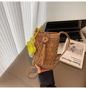 Dettaglio della borsa a tracolla in paglia intrecciata a mano con nappa e ciondolo a margherita